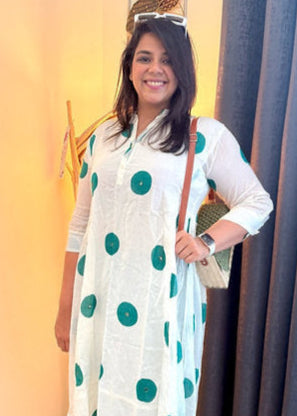 Woman wearing a white kurta with green polka dots and light blue jeans indoors.
