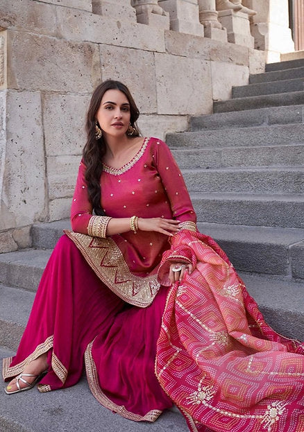 Woman wearing a coral and fuchsia sharara suit with embroidered kurta and pink printed dupatta – ideal for Diwali, Rakhi, Karwachauth, and wedding functions in UAE by Meraki Vastram.