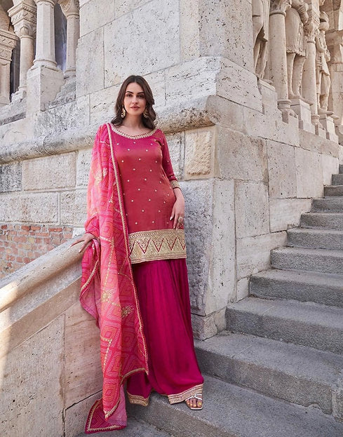 Woman wearing a coral and fuchsia sharara suit with embroidered kurta and pink printed dupatta – ideal for Diwali, Rakhi, Karwachauth, and wedding functions in UAE by Meraki Vastram.