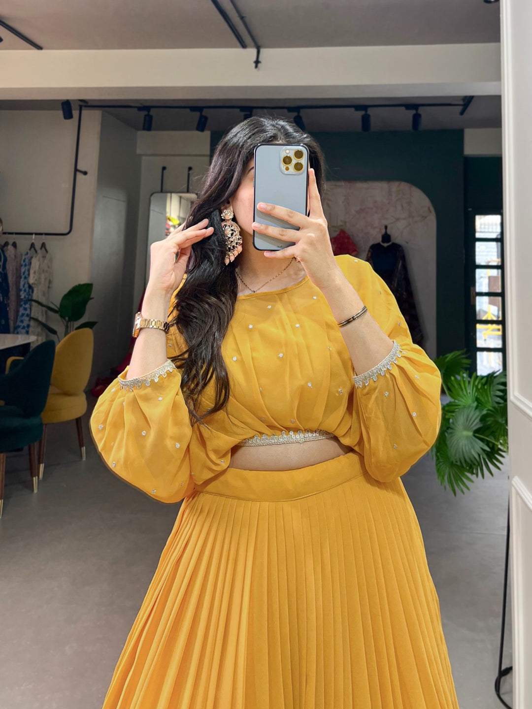 Woman wearing a yellow pleated lehenga with floral embroidery and balloon sleeve blouse taking a mirror selfie- perfect for Haldi, Teej, Diwali, Ganpati and festive celebrations – Meraki Vastram ethnic wear in UAE.
