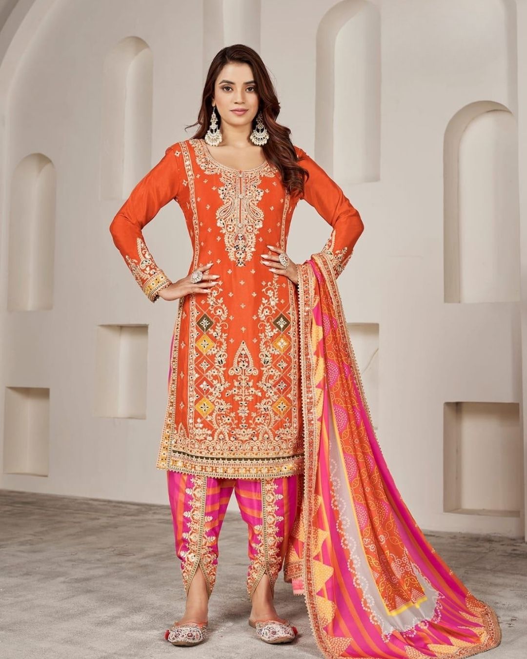Woman wearing an orange embroidered kurta with pink striped salwar and matching dupatta – festive Punjabi suit for Diwali, Karwachauth, Teej & mehendi functions from Meraki Vastram UAE.
